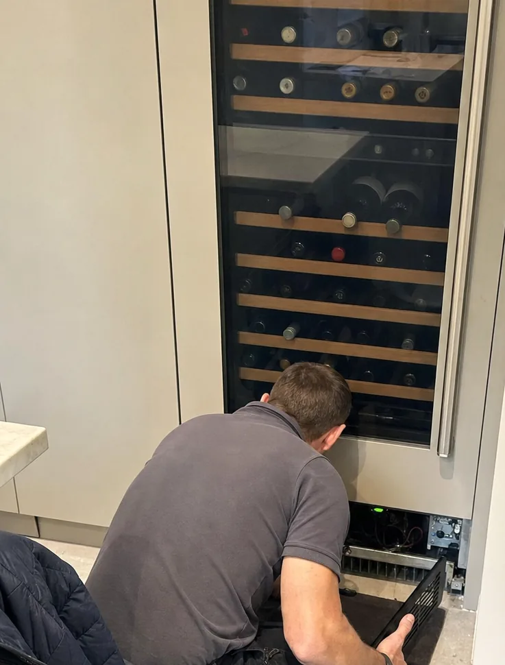 A wine column with its lower grille removed, the technician working at the machine compartment at floor level.