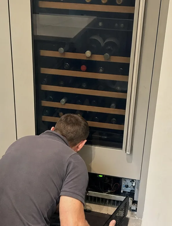 A tight view of a wine column: two zones of bottles on wooden runners, the technician kneeling at the base.