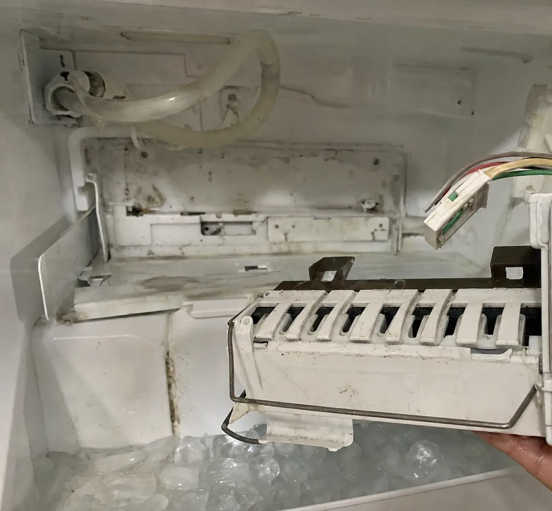 The interior of a freezer compartment with the ice-maker module removed, frost and staining marking the liner behind it.