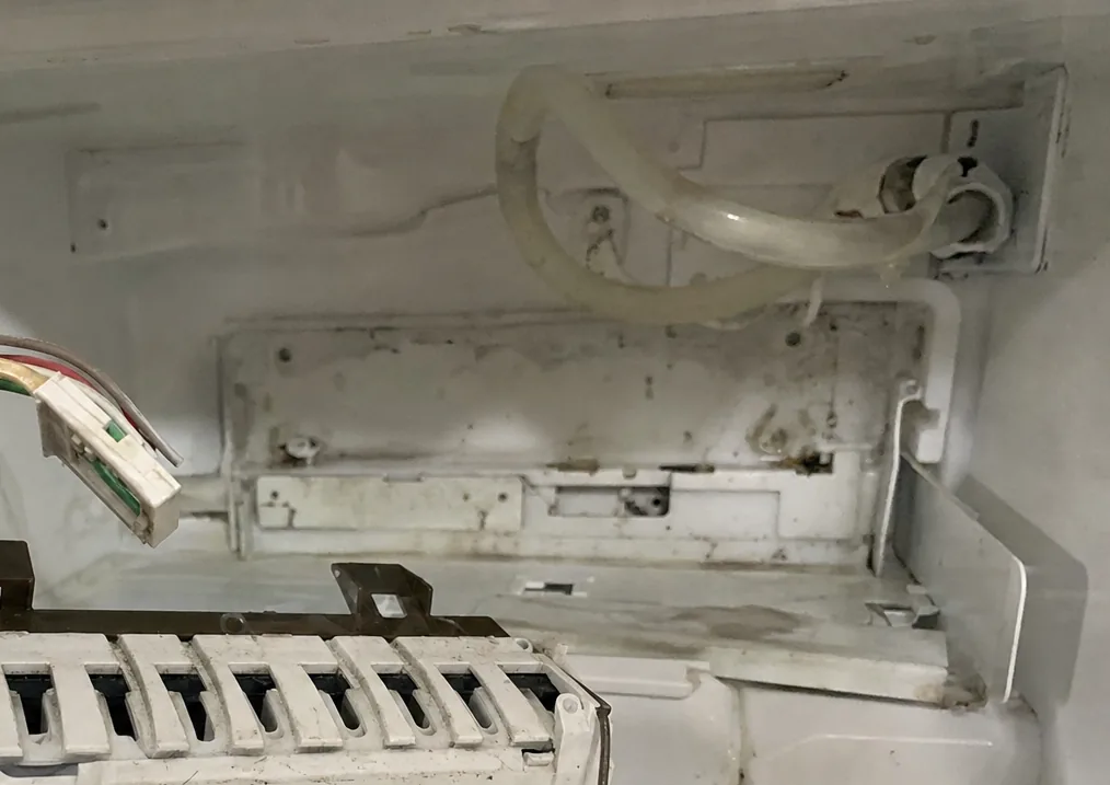 The empty ice-maker bracket and fill tube inside a freezer liner, the module itself lifted clear at the edge of the frame.